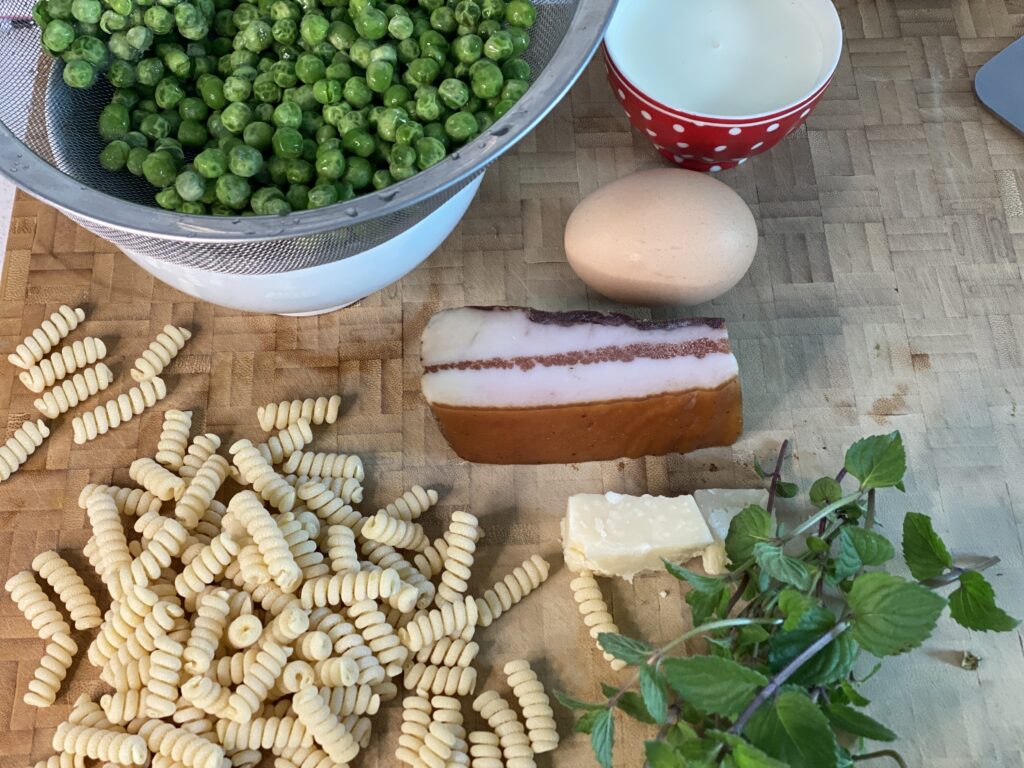 Fusilli, Erbsen, Pancetta, Ei, Minze und Sahne auf Küchenbret