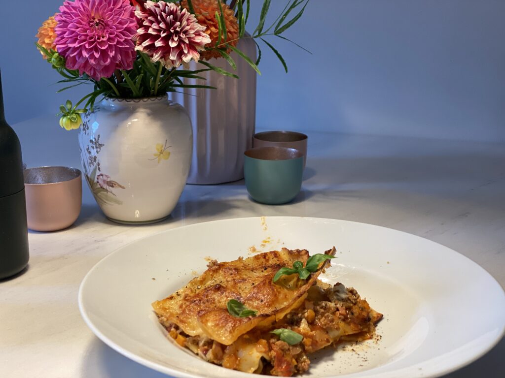 Teller Lasagne Bolognese auf Tisch mit Blumenvase