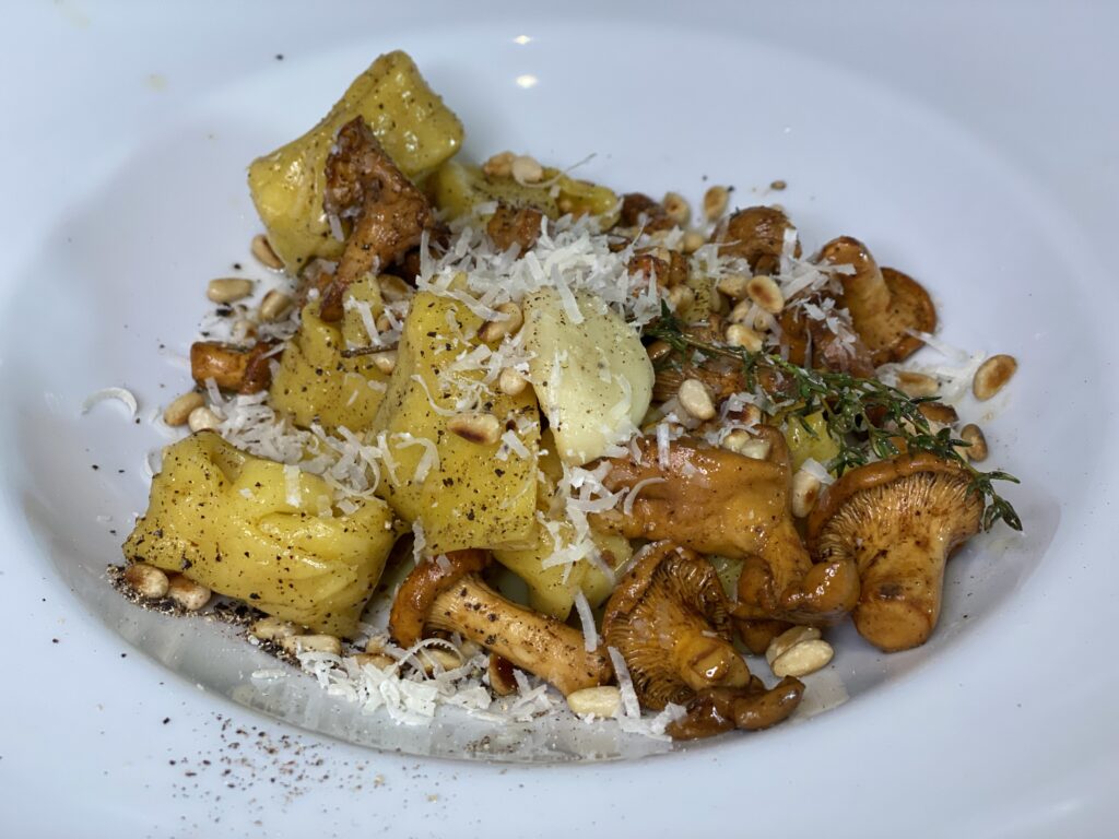 Tortelloni mit Pfifferlingen, Pinienkernen und Parmesan auf tiefem Teller
