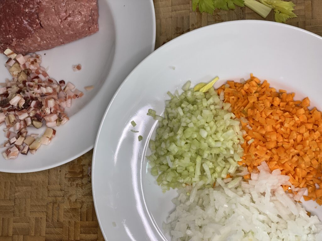 Teller mit klein gewürfelten Möhren, Sellerie und Zwiebel und Teller mit Hackfleisch und Pancetta 