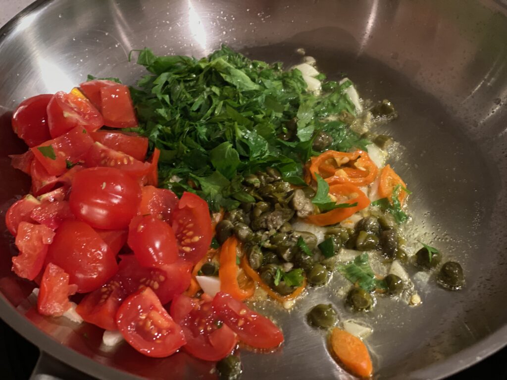 Kapern, Knoblauch, Chili, Petersilie und Tomaten in Pfanne